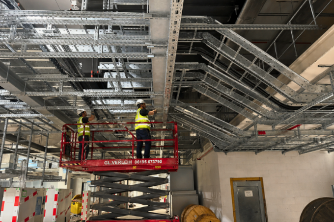 Instaladores trabajando en altura sobre plataformas elevadoras, revisando cableado eléctrico sobre bandejas portacables metálicas PohlCon en el techo técnico de una nave industrial.
